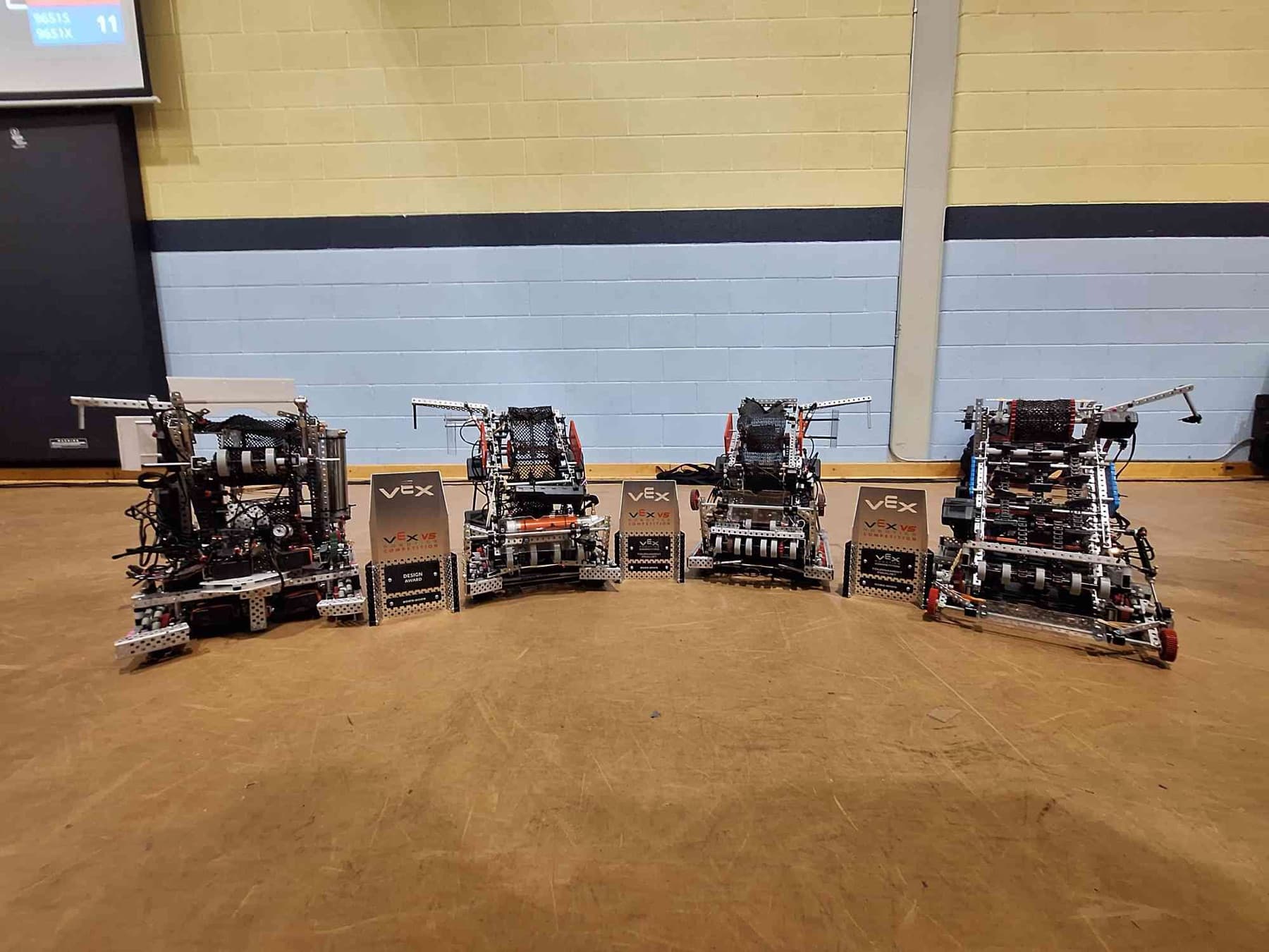 Four UTS Robotics VEX robots lined up on a gym floor next to their award plaques