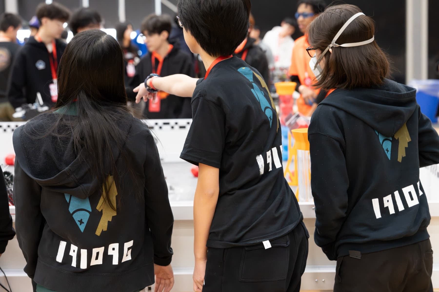 Three 19109G members in team hoodies watching a match from behind the field
